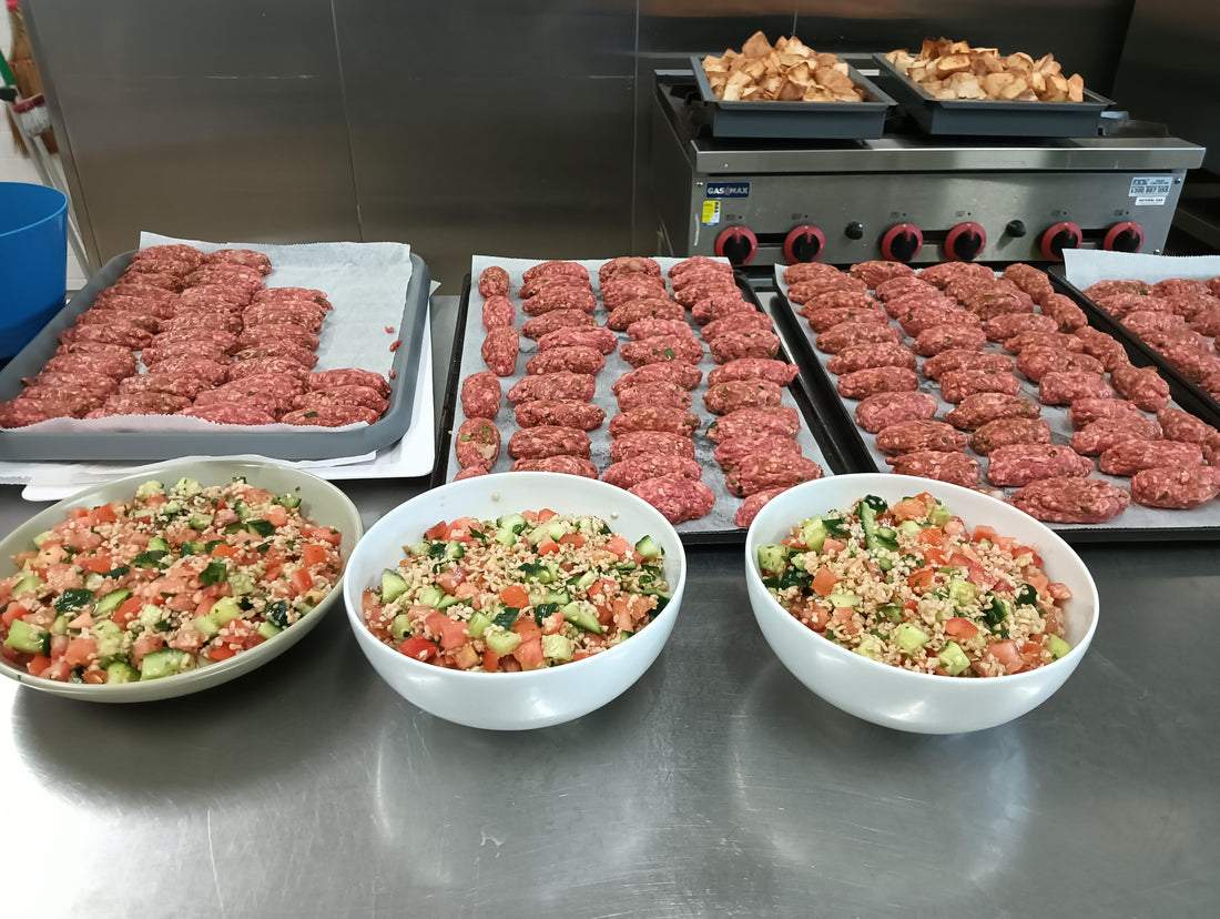 Multiple trays with beautiful chef made lamb kofta, next to white bowels of fresh Greek salad.